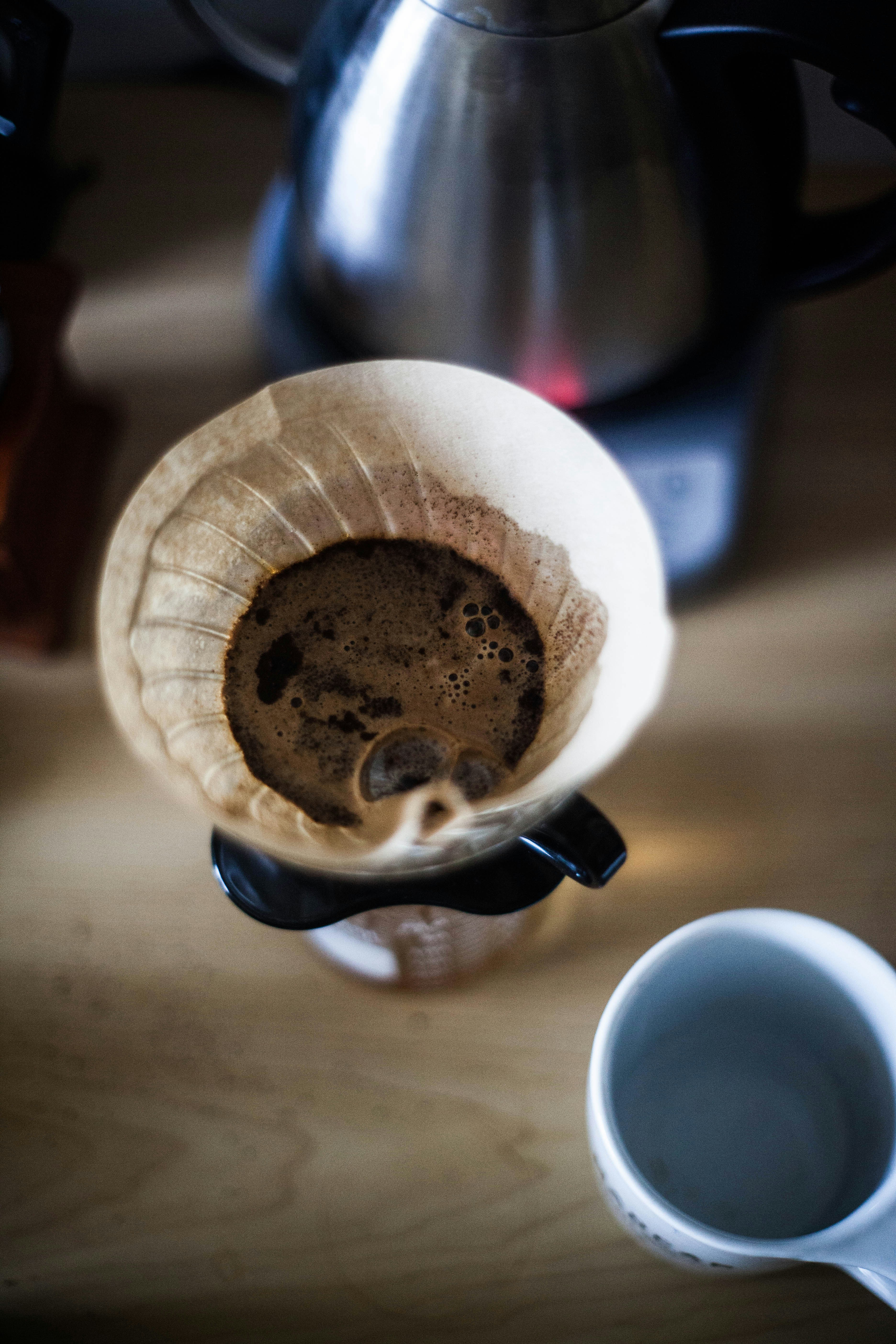 Close-up of pour-over coffee dripping into ceramic cup, steam rising, warm cream tones, artisan brewing ritual