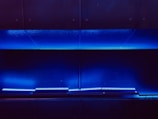 A dark, minimalist scene with a series of horizontal blue LED lights illuminating a sleek metallic surface. The ambient lighting casts a soft, futuristic glow.