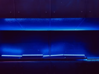 A dark, minimalist scene with a series of horizontal blue LED lights illuminating a sleek metallic surface. The ambient lighting casts a soft, futuristic glow.