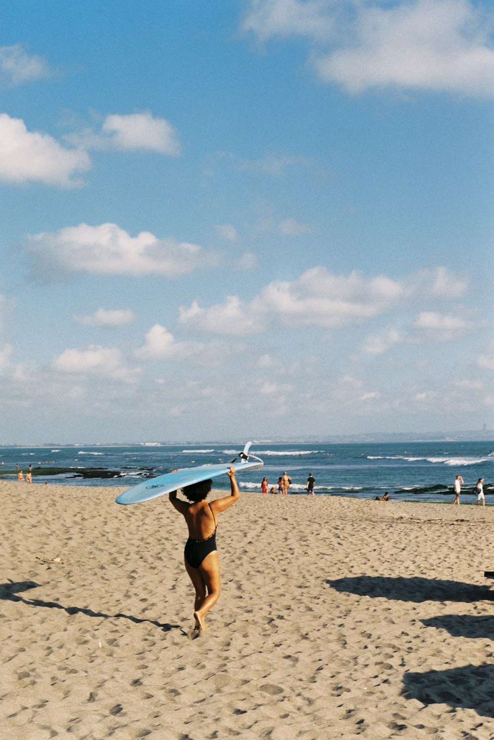 woman in white bikini holding white surfboard walking on beach during daytime