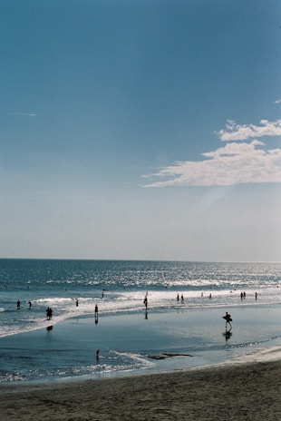 Wide shot of a famous Los Angeles beach with sunbathers and surfers under a clear blue sky.