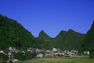 A cozy village home nestled among lush green hills under a clear blue sky.