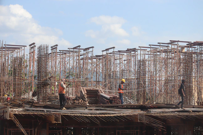 A group of foreign workers in safety gear at a bustling construction site under a deep blue sky.