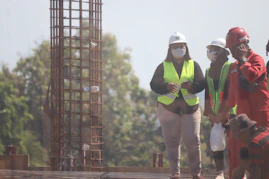 A group of professional workers wearing safety gear collaborating on a construction site, with the company logo visible on their uniforms.