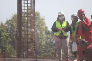 A group of professional workers wearing safety gear collaborating on a construction site, with the company logo visible on their uniforms.