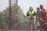 A group of construction workers wearing safety gear, including helmets and reflective vests, are gathered near a vertical metal structure on a construction site. Trees and greenery are visible in the background.