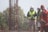 A group of construction workers wearing safety gear, including helmets and reflective vests, are gathered near a vertical metal structure on a construction site. Trees and greenery are visible in the background.