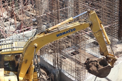 yellow excavator near gray metal fence during daytime