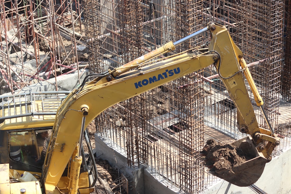 yellow excavator near gray metal fence during daytime