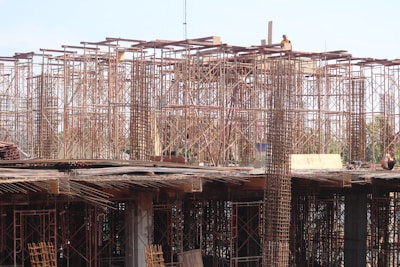 Scaffolding and construction materials form a complex structure, with metallic frameworks rising vertically. Several workers are present, engaging in construction tasks on an unfinished building.