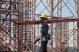 man in grey jacket and yellow hard hat standing on orange metal ladder