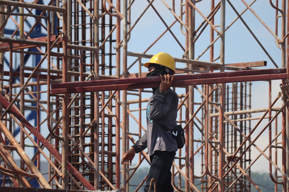 man in grey jacket and yellow hard hat standing on orange metal ladder