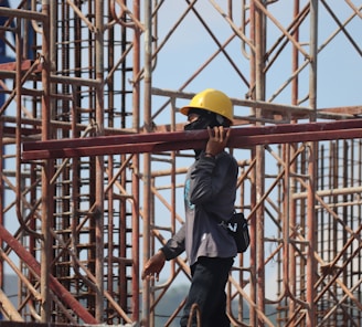 man in grey jacket and yellow hard hat standing on orange metal ladder