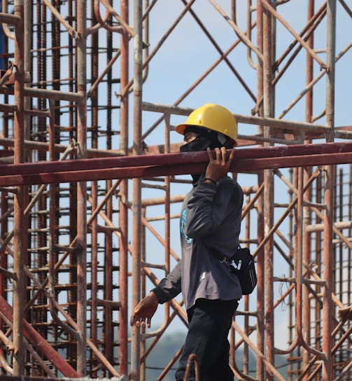 man in grey jacket and yellow hard hat standing on orange metal ladder