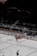 An ice hockey match in a stadium with players in red and white uniforms on the ice rink. Advertisements and boards line the rink's perimeter. A large blimp with Cyrillic writing hovers above the seating area.
