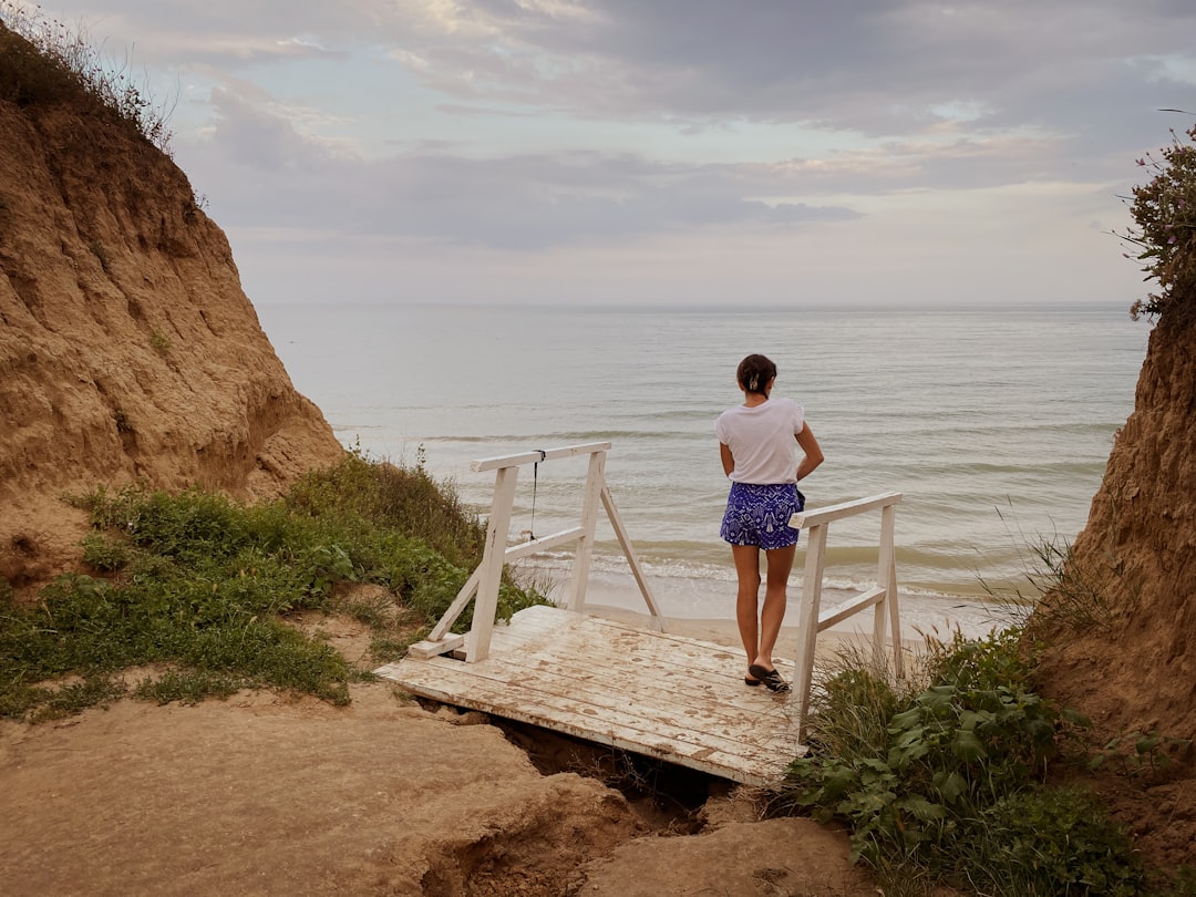 man in white t-shirt and blue shorts standing on white wooden staircase near body of near near near near