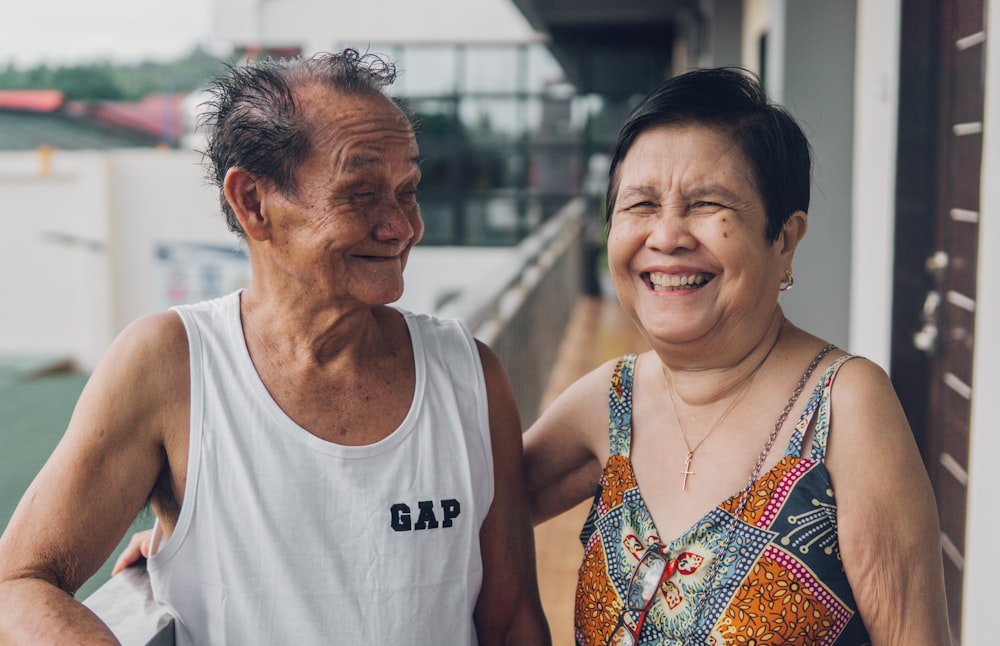 man in white tank top smiling beside woman in orange and white floral sleeveless top