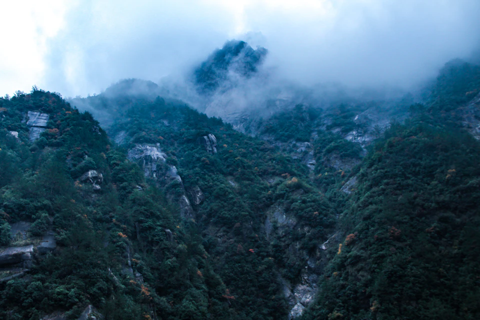 Mountainous landscape with foggy sky and lush green vegetation under soft, overcast light conditions