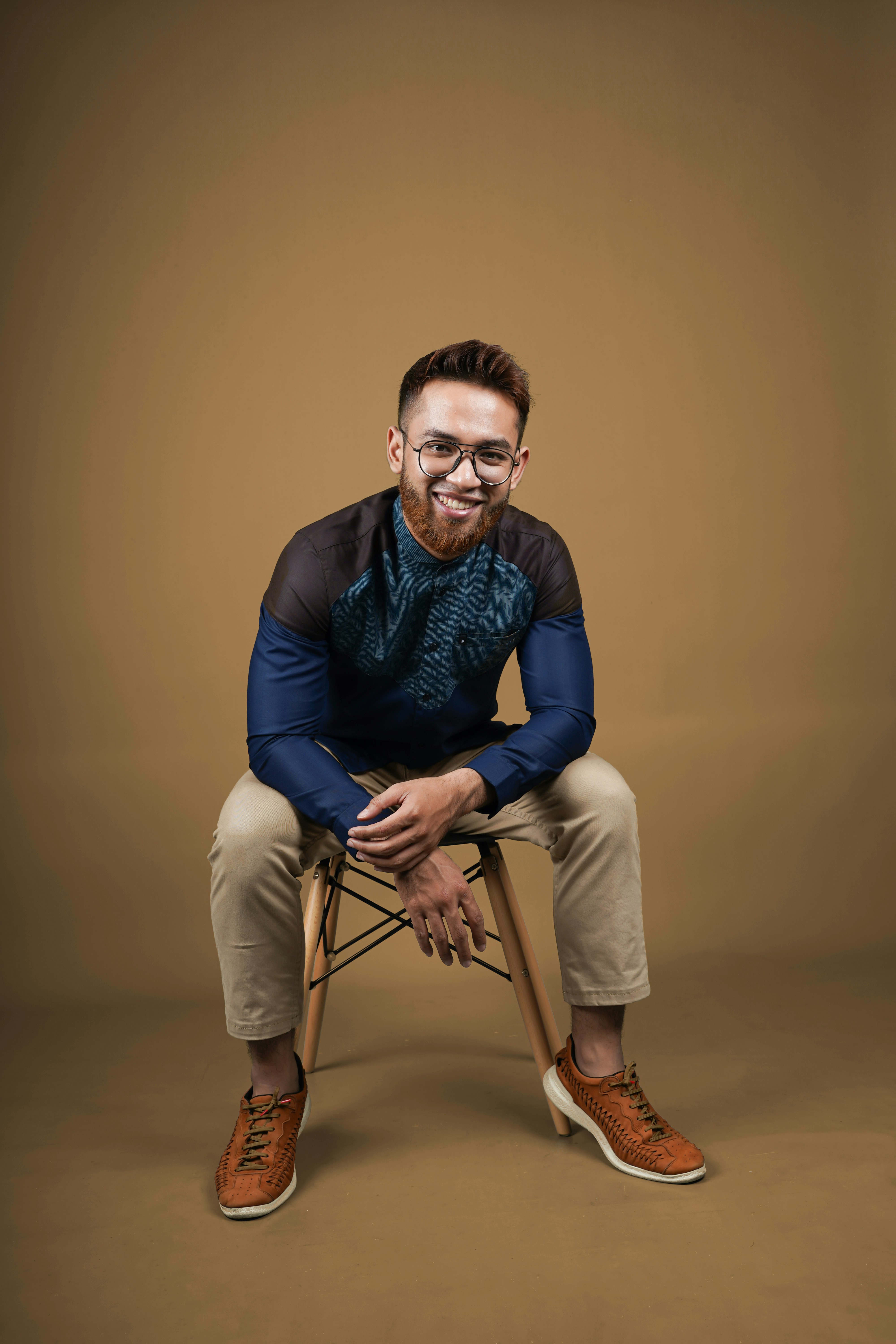 Mann in blauem Langarmhemd und beiger Hose sitzt auf braunem Holzstuhl