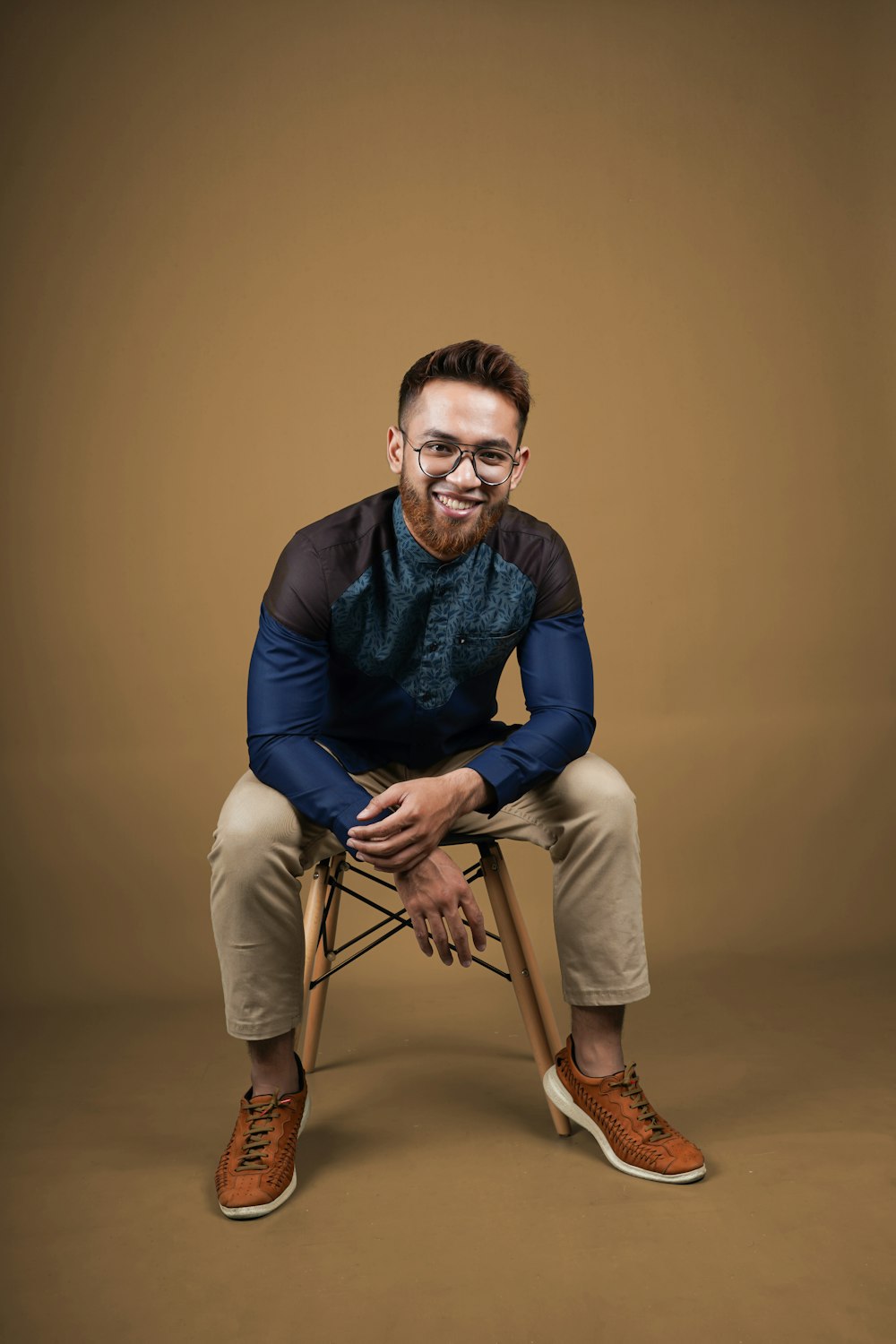 man in blue long sleeve shirt and beige pants sitting on brown wooden chair