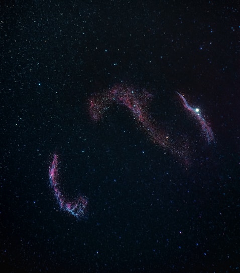 A vast expanse of outer space with numerous stars scattered across a dark background. In the center, there is a vibrant display of cosmic gas and dust, creating a nebula with colorful hues, predominantly in shades of red and blue.