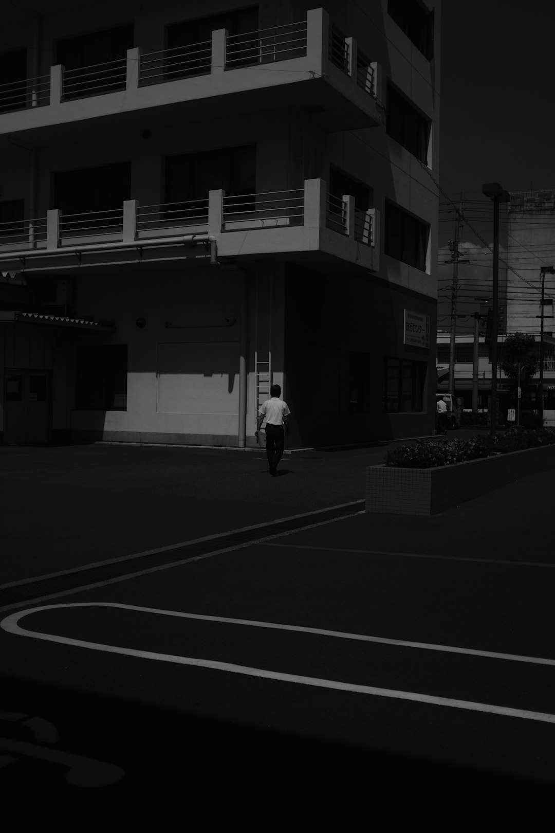 grayscale photo of man walking on sidewalk near building