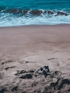 A pair of durable water shoes placed on a sandy beach with gentle waves in the background.