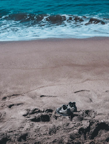 Close-up of sleek aqua shoes resting on wet sand near gentle waves.