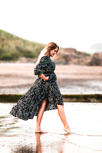 woman in black and white floral dress standing on seashore during daytime