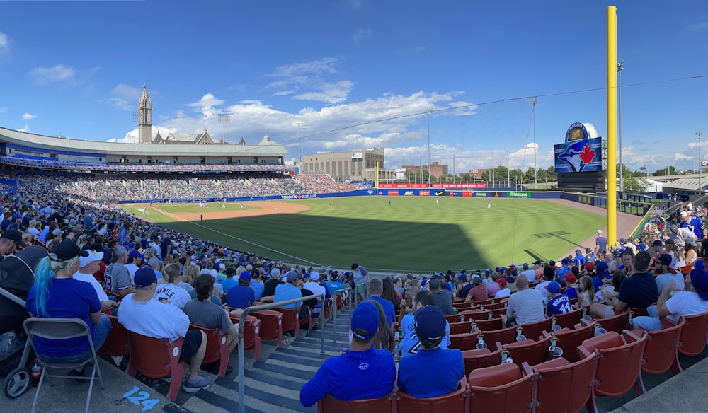 Gente sentada en sillas de estadio viendo un partido de béisbol durante el día