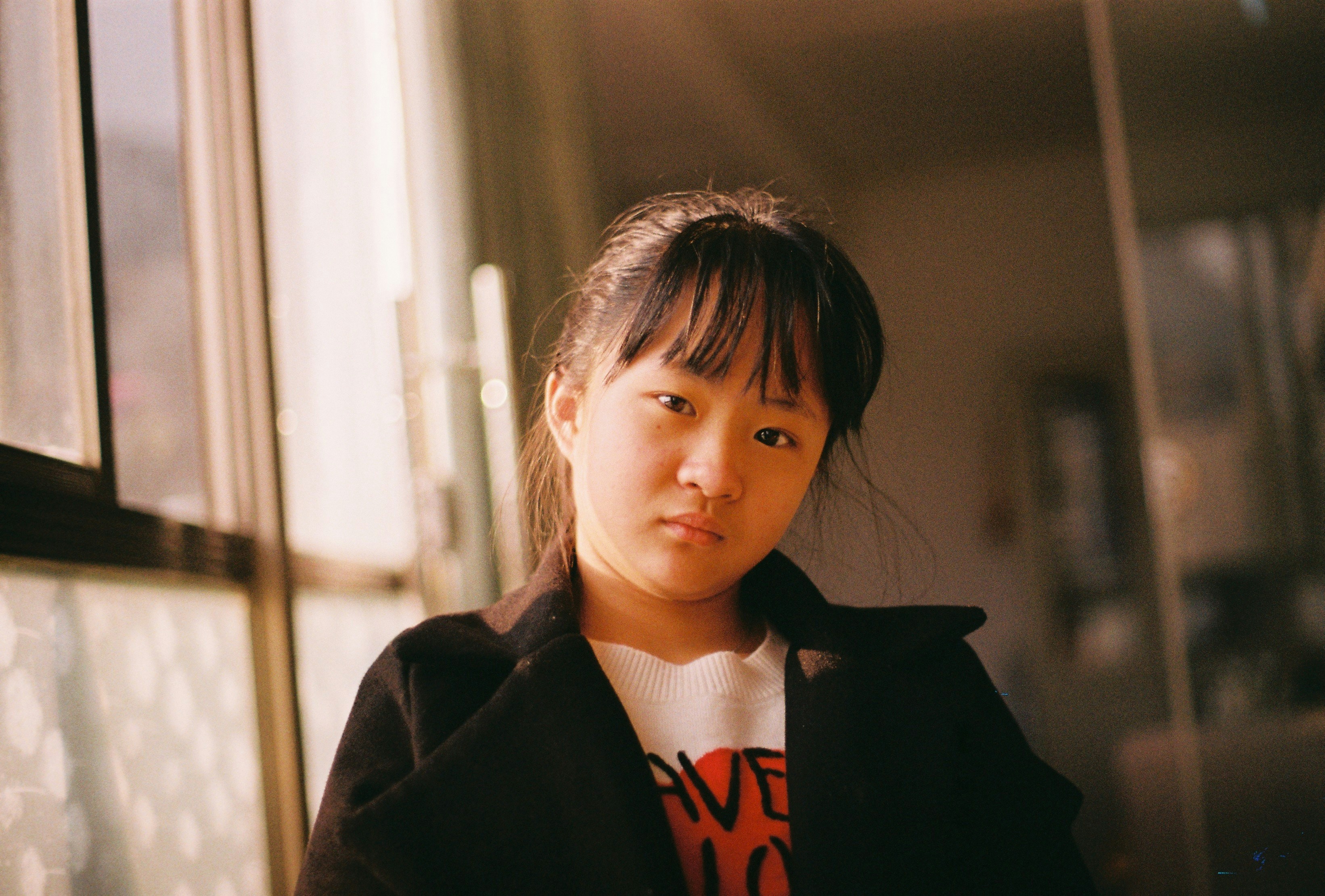 girl in black coat standing near window