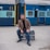 man in black blazer sitting on black metal bench beside blue train during daytime