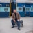 man in black blazer sitting on black metal bench beside blue train during daytime