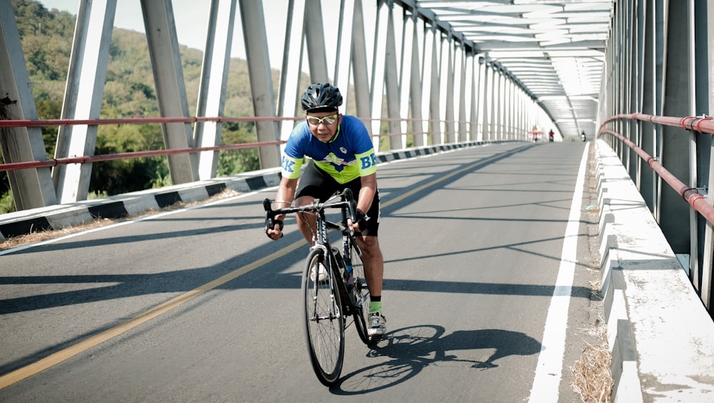 uomo in camicia verde che cavalca in bicicletta sul ponte durante il giorno