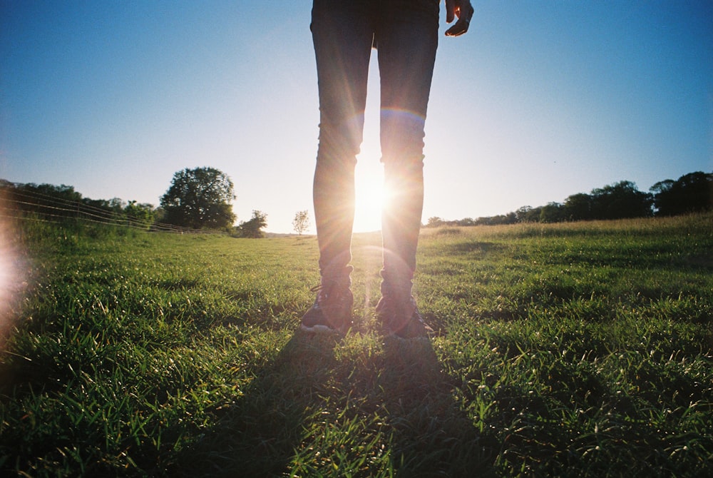pessoa em calças pretas em pé no campo de grama verde durante o dia