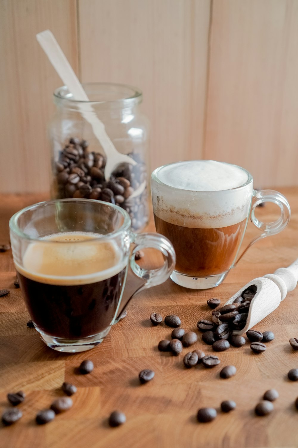 Taza de vidrio transparente con granos de café sobre mesa de madera marrón