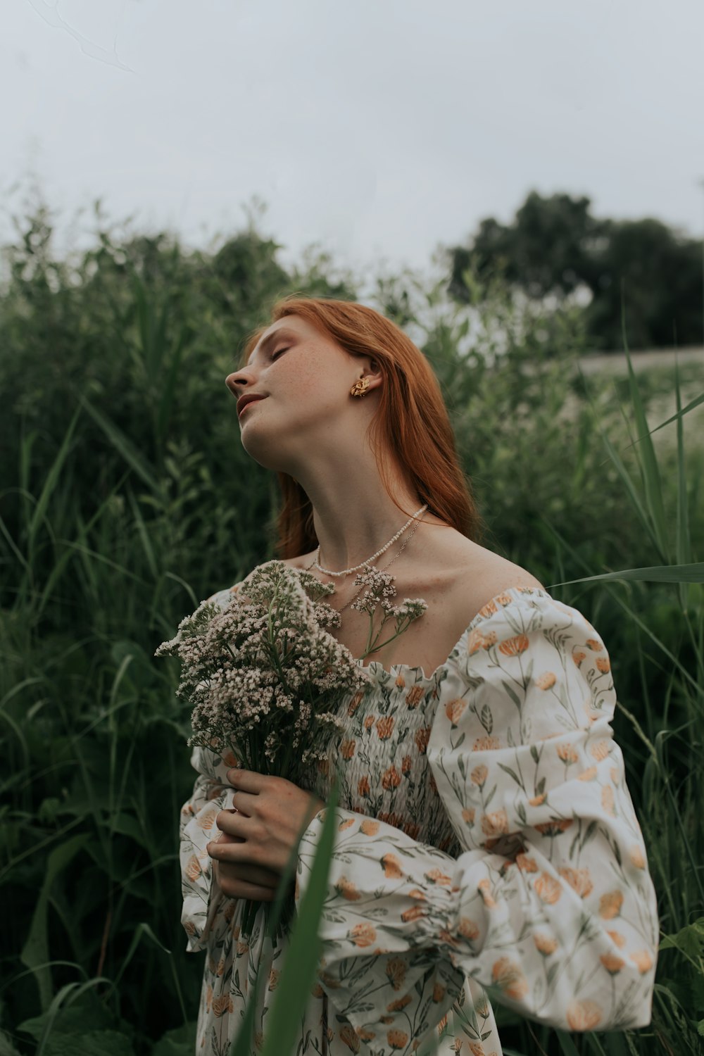 donna in abito bianco e marrone floreale con spalle scoperte in piedi sul campo di erba verde durante il giorno