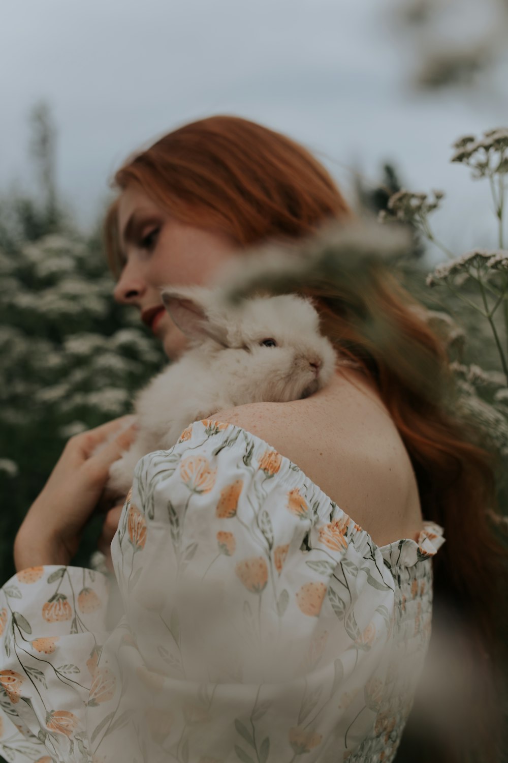woman in white and orange floral dress holding white fur animal