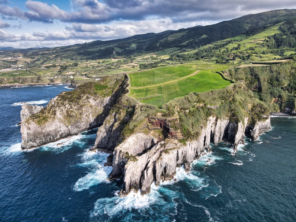 green grass field on rocky mountain beside sea under white clouds and blue sky during daytime