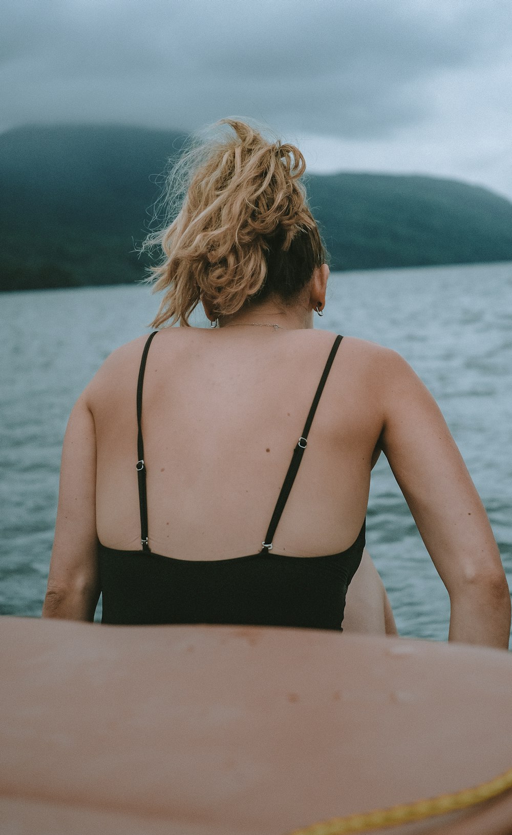 Mujer en la parte superior del bikini negro sentada en el muelle de madera marrón durante el día