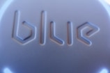 The image displays a close-up view of a surface with the word 'blue' embossed in a modern, geometric font style. The texture appears smooth with a play of light and shadow enhancing the three-dimensional effect of the lettering.