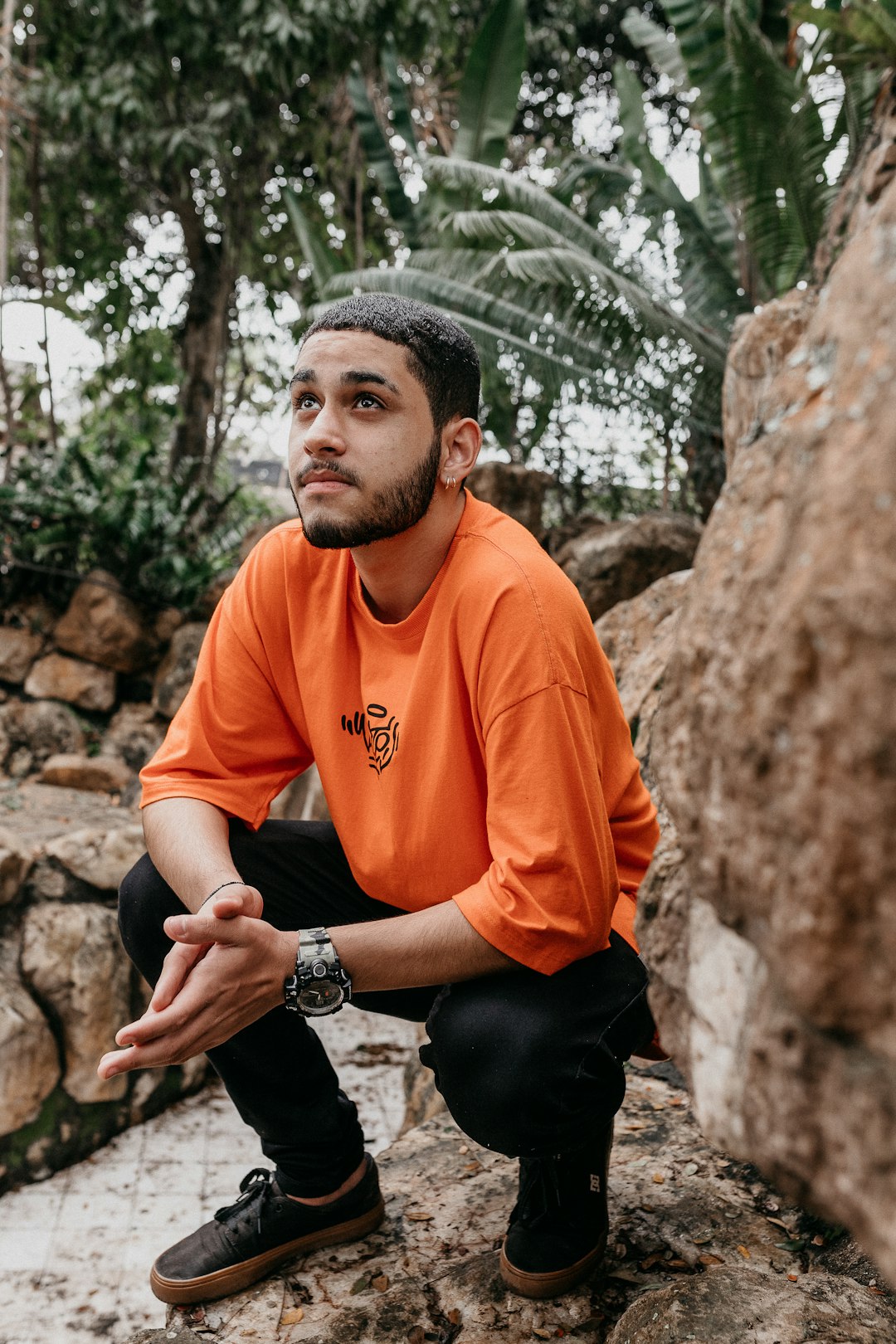 man in orange crew neck t-shirt and black pants sitting on rock during daytime