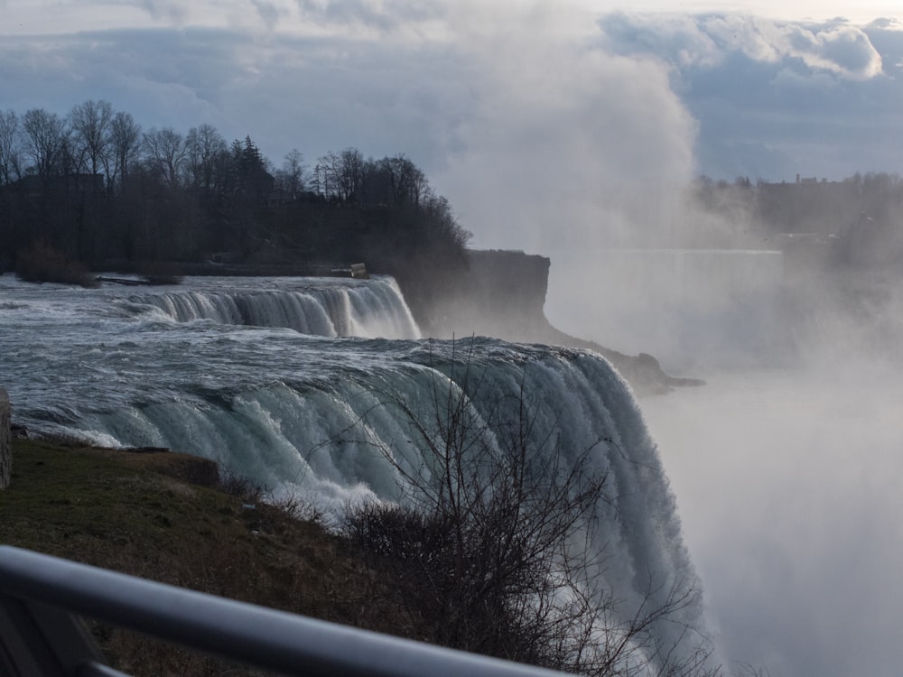 waterfalls near green trees under white clouds during daytime