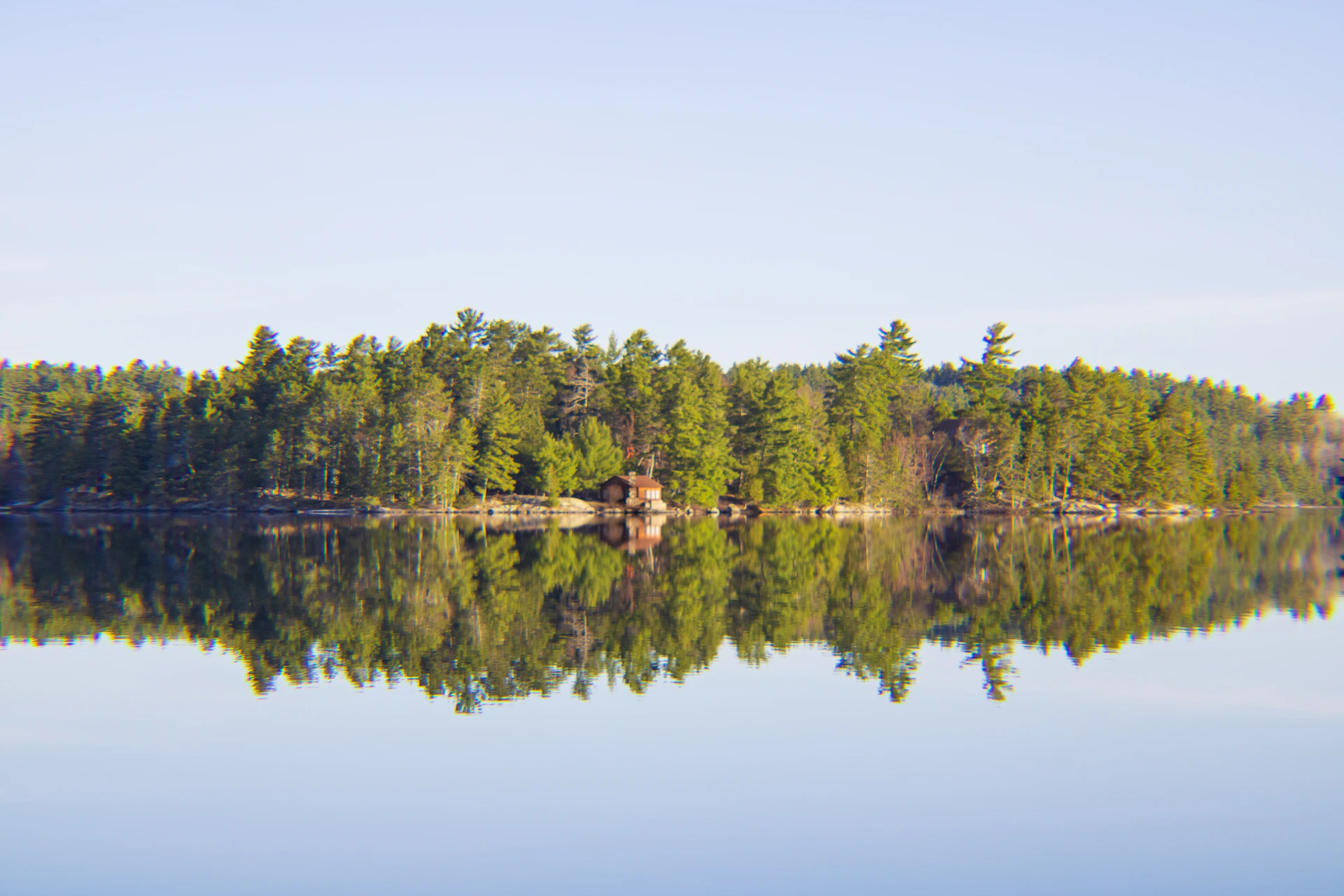 A serene Finnish lake at sunset with a wooden sauna cabin nestled among tall pine trees.