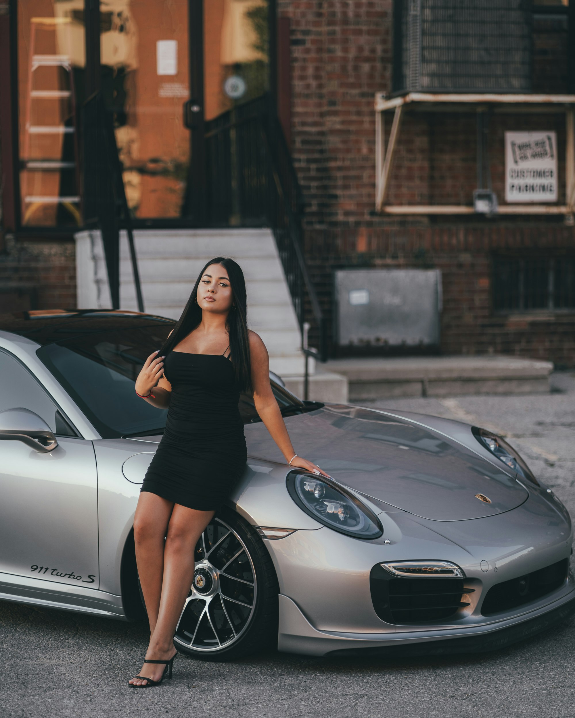 woman in black dress leaning on white car