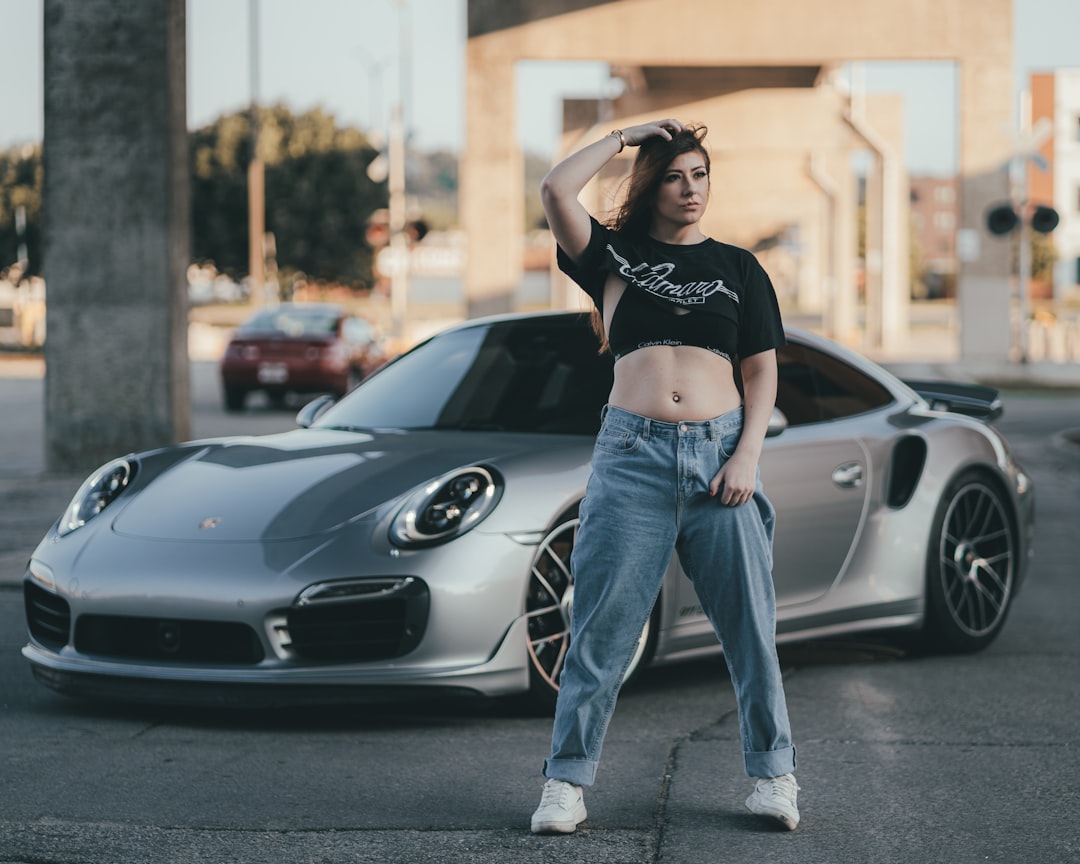 woman in black crop top and blue denim jeans standing beside gray car during daytime