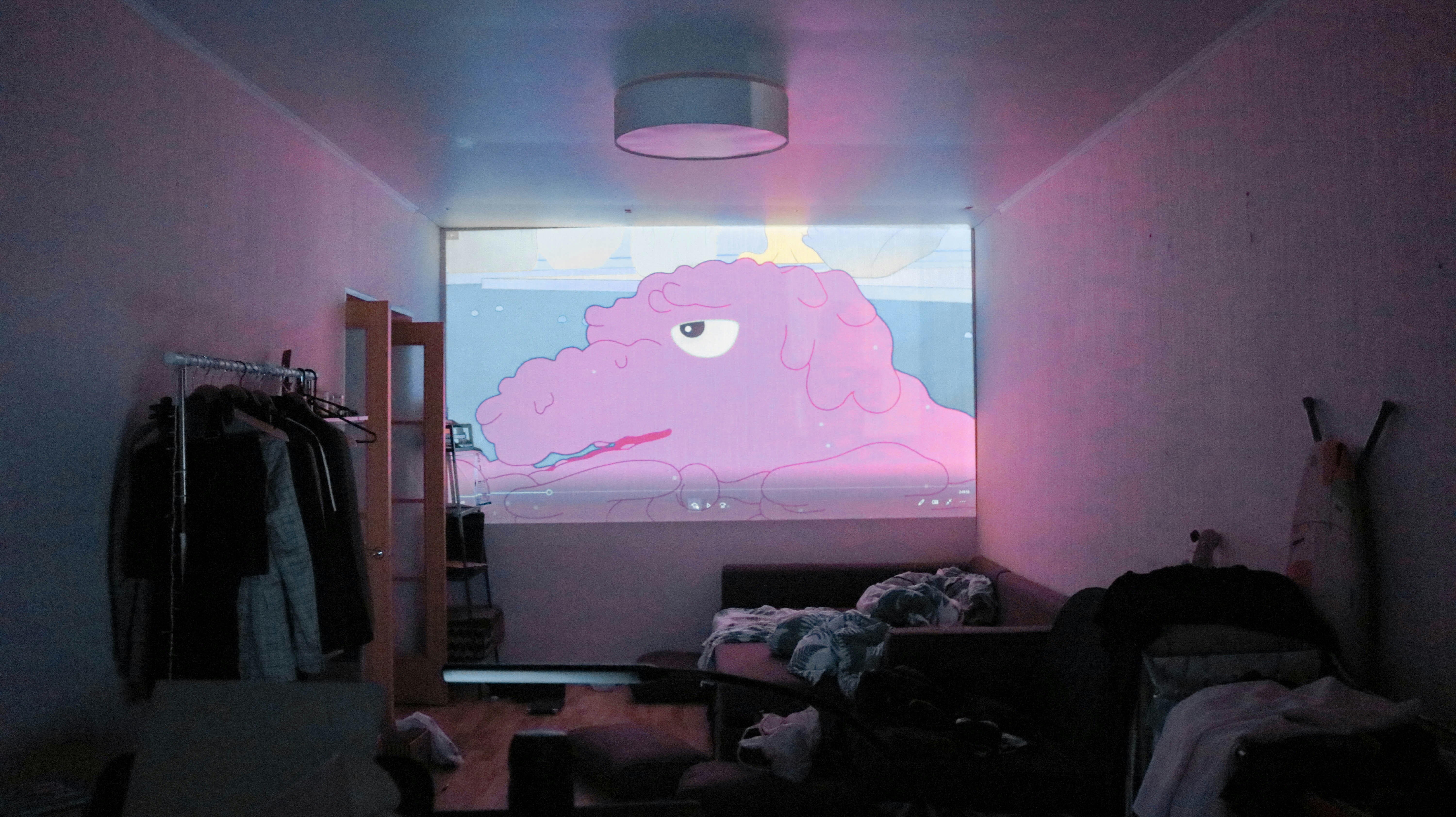 A large flat screen tv displays a pink dog from a video that is using royalty free cartoon music for animated videos.