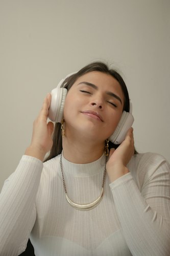 Close-up of headphones resting on a laptop keyboard next to a phone displaying a music playlist