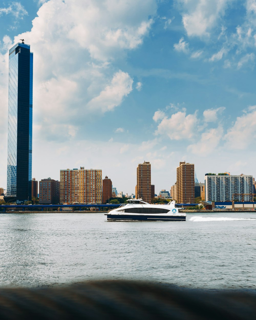 white and black boat on sea near city buildings under blue and white sunny cloudy sky