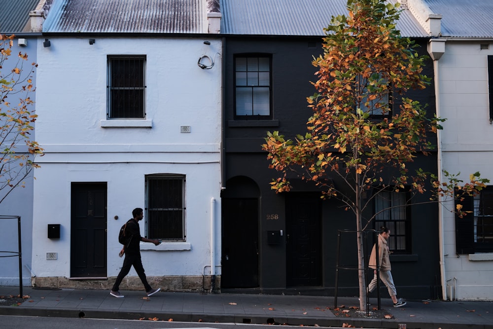 man in black jacket walking on sidewalk near white concrete building during daytime